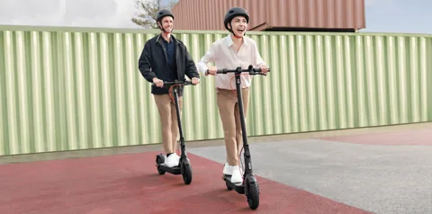Deux personnes casquées qui roulent en Xiaomi Electric Scooter 4 Pro (2e génération) devant un mur de tôle
